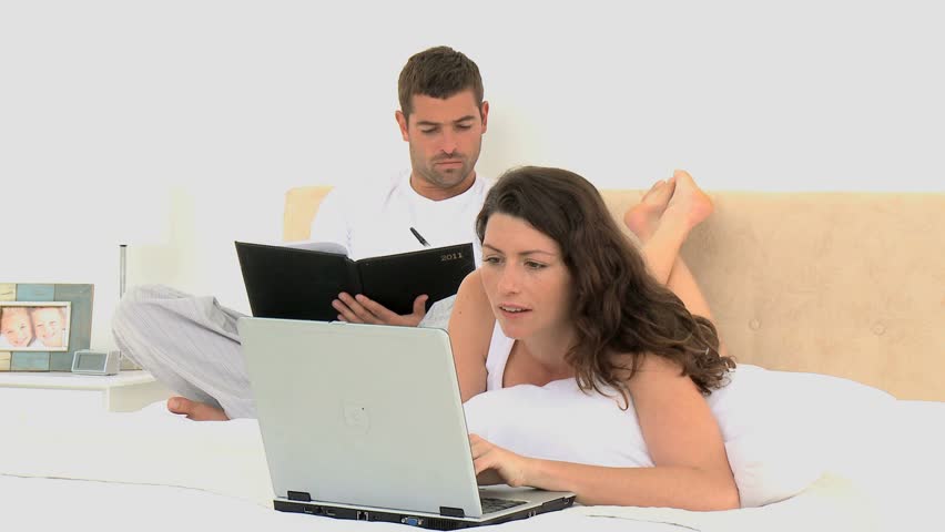 Couple laughing after watching a video on the laptop lying on the bed at home