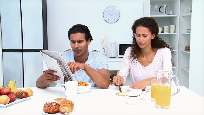 Man reading newspaper while having breakfast with his girlfriend