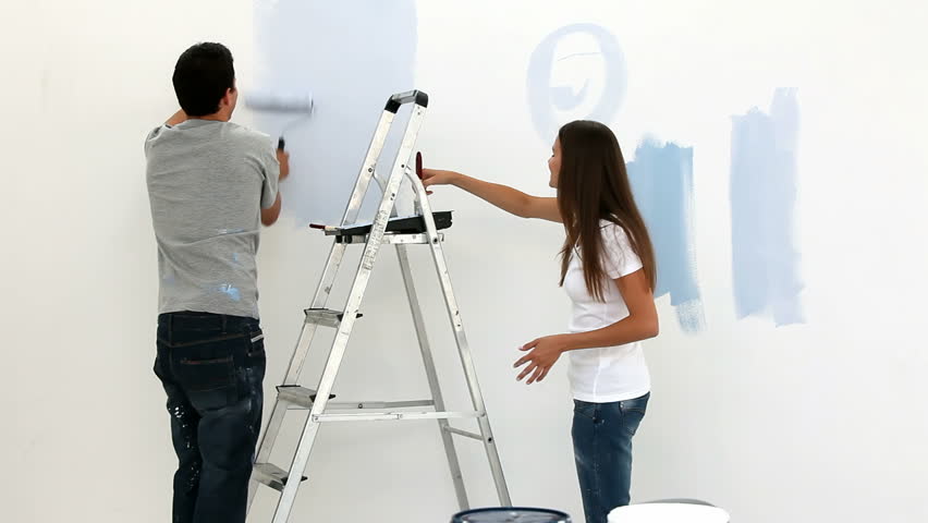 Happy couple painting wall in blue in their bedroom