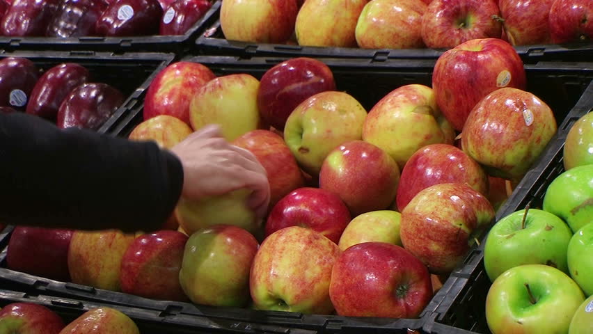 Woman selecting fresh red apples in grocery store produce department.