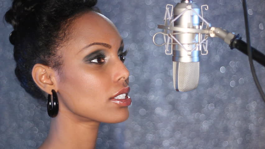 Studio singer.  Attractive young woman sings into a professional, condenser microphone.  
