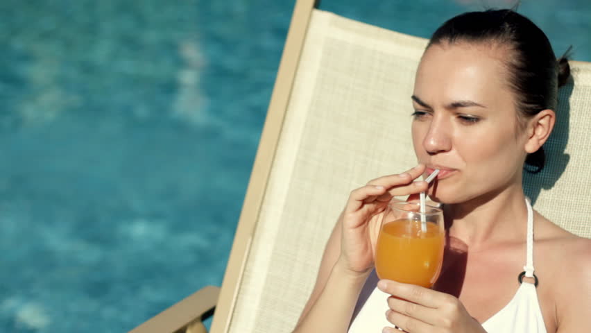 Woman lying by the pool and drinking exotic drink 