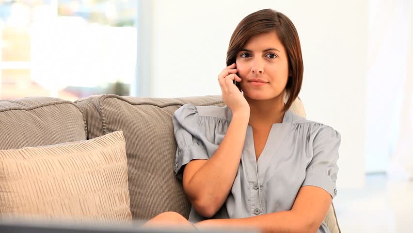 Brunette woman speaking on a smartphone on her sofa
