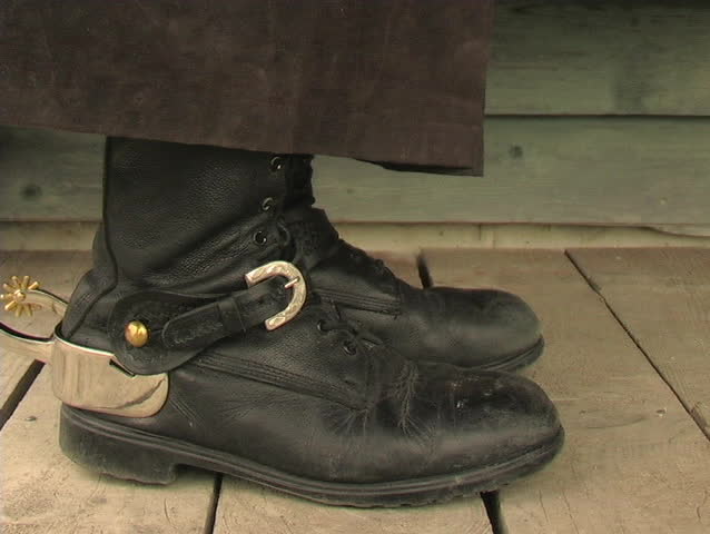 CLOSE-UP OF COWBOY BOOTS WALKING ON THE BOARDWALK OF A WESTERN TOWN.