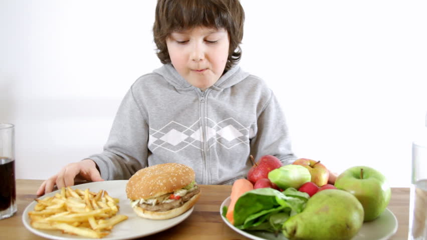 Young boy choosing fast food instead of vegetables and fruits