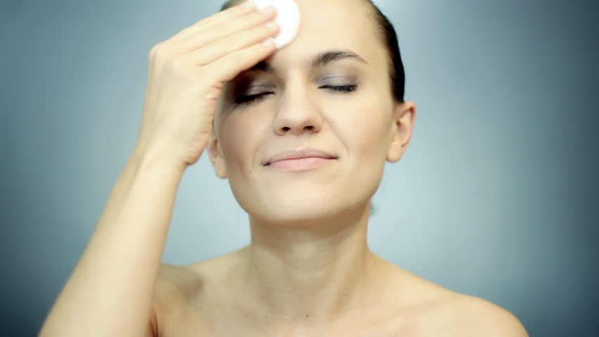 Young attractive woman cleaning her face, grey background