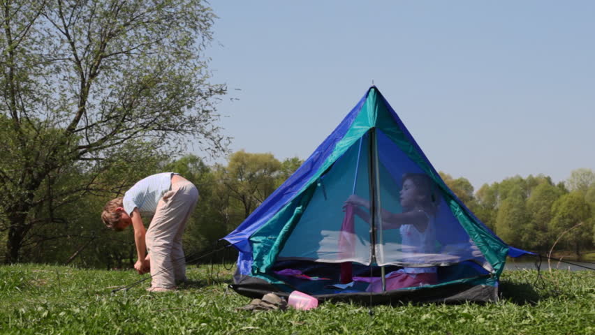 boy strengthens tent cables, little girl opens zipper mosquito net in forest summer
