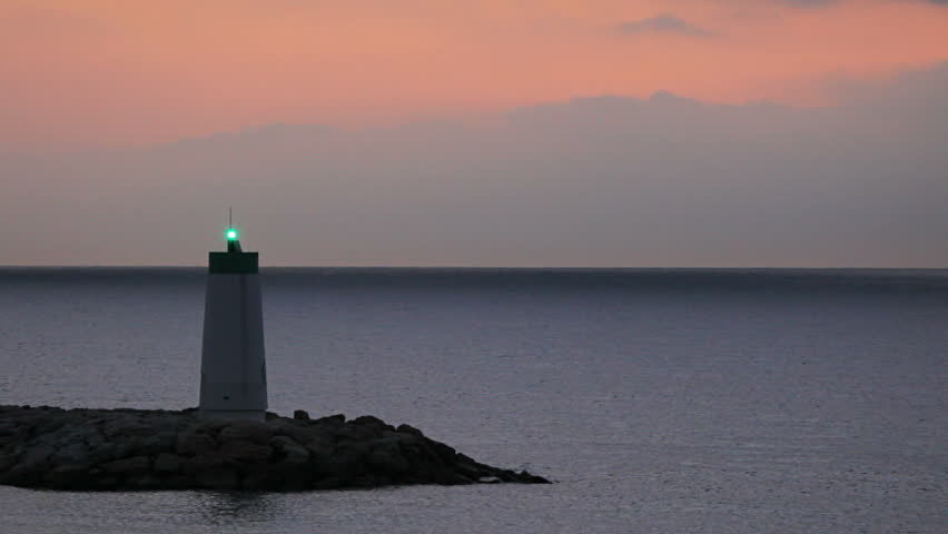 Green navigation beacon flashing on tower with colorful morning clouds.  