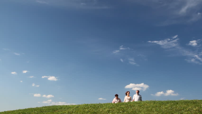 elderly couple by hand with adult daughter on grassy hill against sky in summer