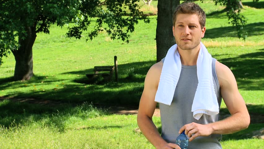 Pretty man drinking water after sports in a park