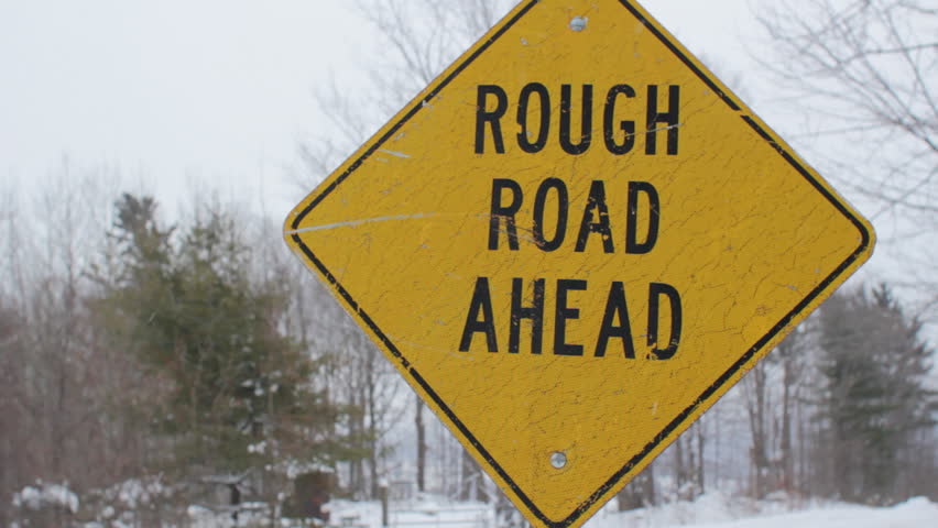 Rough road ahead. Yellow, diamond shaped sign warns of rough road ahead. Light snow falling. Winter road in rural Ontario, Canada. 