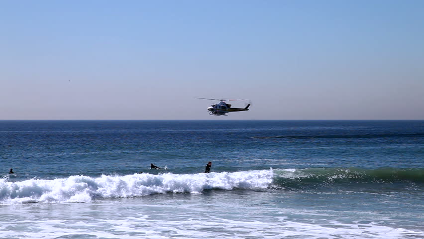 Two coast guard crew members jump out of a helicopter into the pacific ocean.