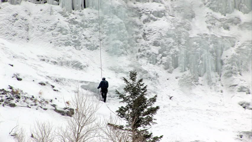 Video pan up of ice climbers climbing ice flow at Bridal Vale Falls in central Utah. Steep rock ledges with frozen waterfall. Athletic sport in cold weather. Wasatch Mountain range. 