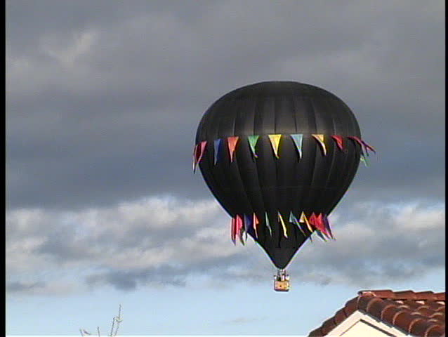 A black hot air balloon with multi-colored streamers makes a low pass across Albuquerque rooftops at the annual Balloon Festival