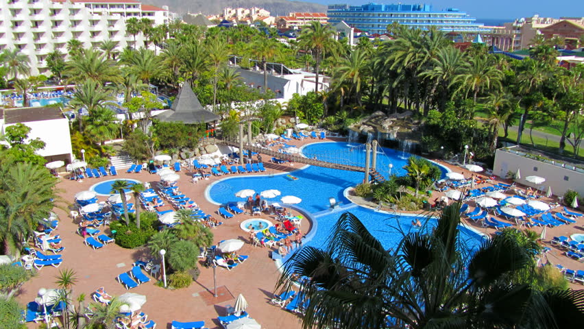 swimming pool with waterfall, lounge chairs, umbrellas, palm trees and a panorama of the city - timelapse