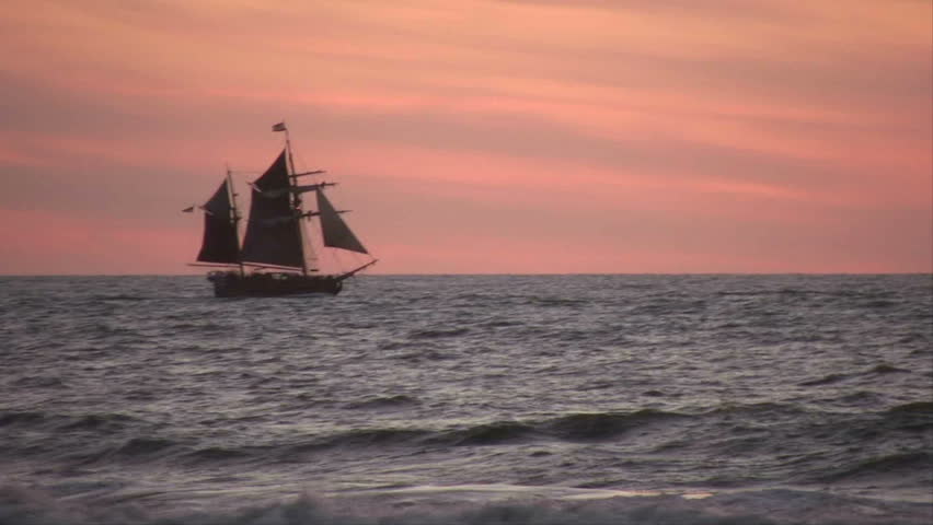 A tall ship sailing across the sea at sunset.