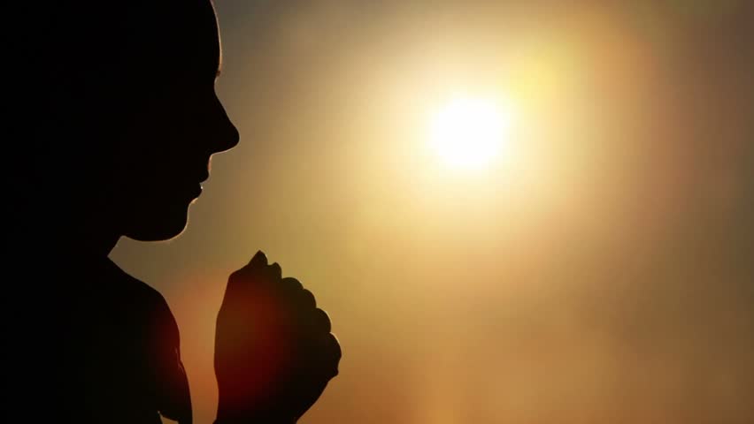 Silhouette of woman head with sunshine behind, holding two fists together, then bowed head