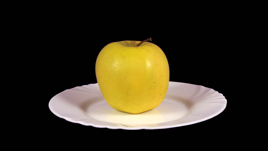 Apple, Golden Delicious, being eaten, turning on a white plate, with the black background.