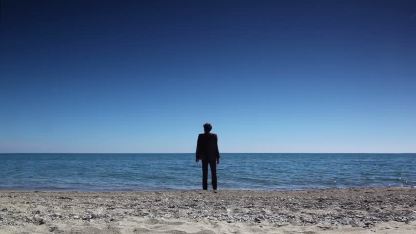 Man in brown suit stand on beach and rises hands, then walked and immersed sea water and swam, at summer sunny day
