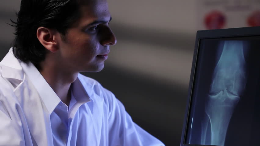 Doctor looking at x-ray image of a knee on a computer, dolly shot.