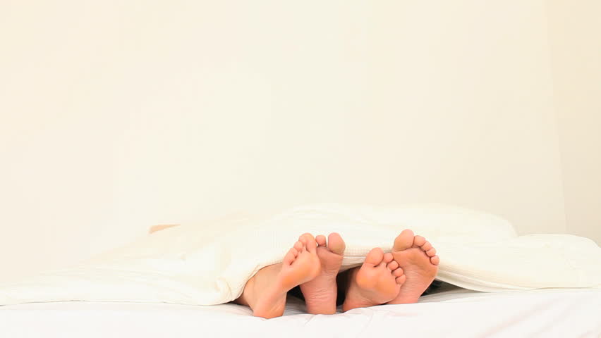 Two pairs of wobbling feet under a blanket in a bedroom