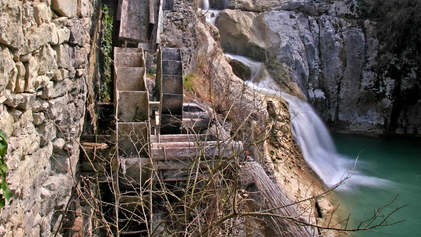Old wooden water mill and the cascade of a falling river into the emerald lake