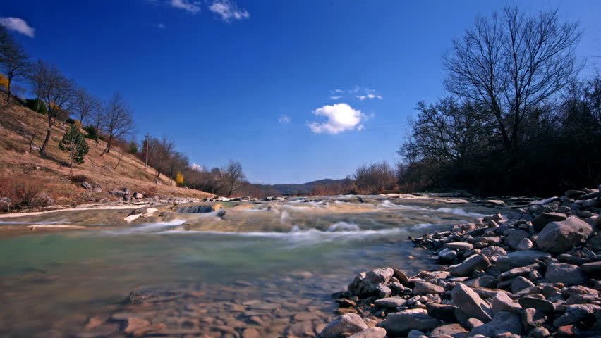 River flowing under the blue sky with the pebble coast