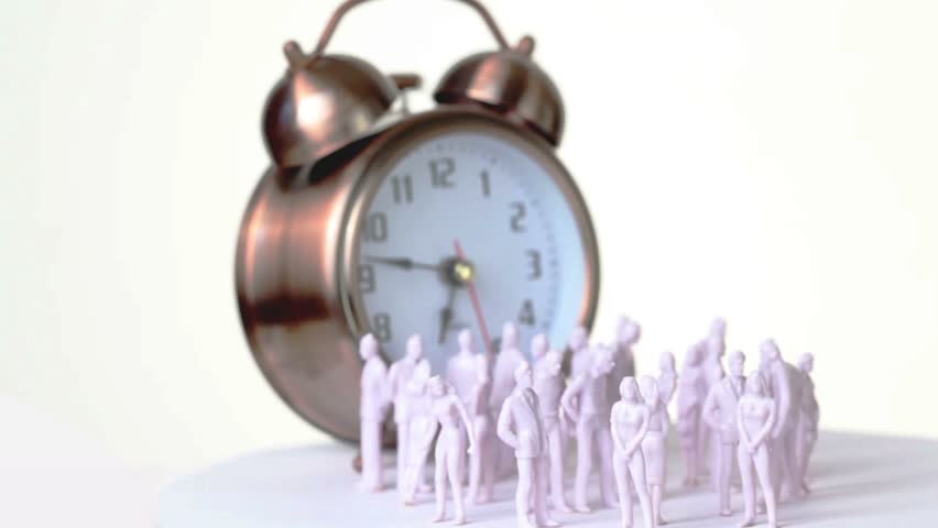Group of little uncolored toy men and women stand in front of big clock which ringing, all composition rotates