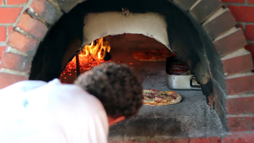 Pizza being baked in a wood fire brick oven in a restaurant. HD 1080i.
