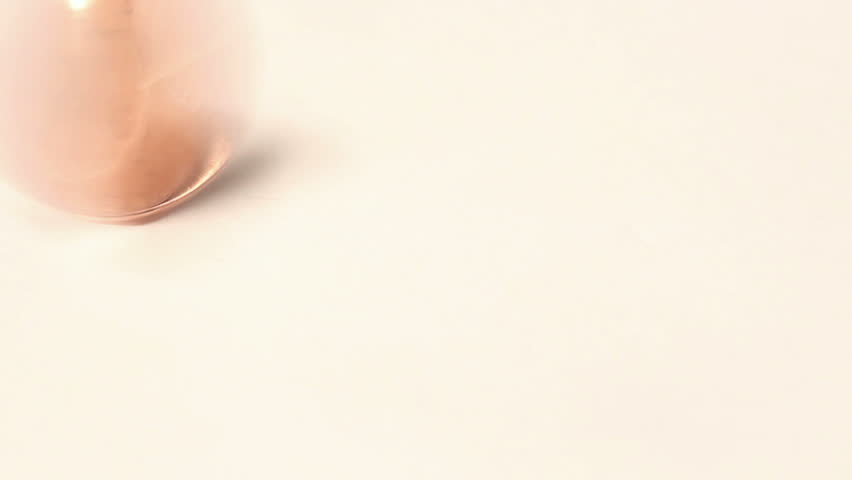 Close up of a spinning United States One Cent piece (penny) and coming to a stop heads up in the corner of the frame on a white background.