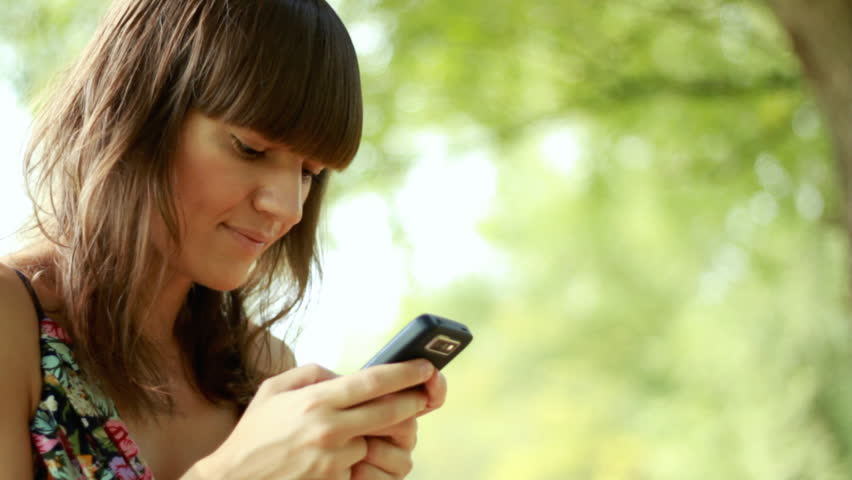 Happy young woman sending sms, texting in the park