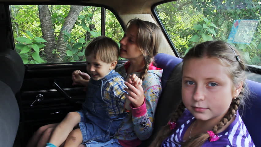 two sisters are happy to sit in back seat car, eldest girl is playing with little brother on his knees, then car drives away 