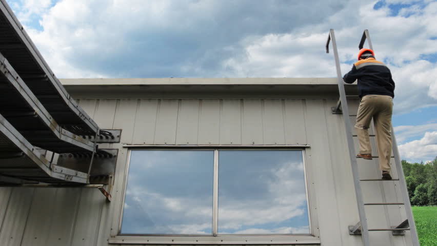worker goes at roof of house and climbs down metal ladder