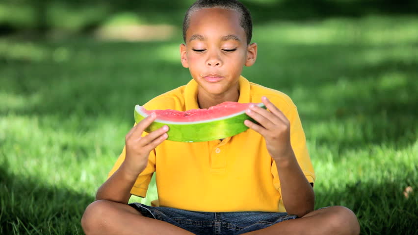 Young african american boy enjoying a refreshing slice of water melon in his garden