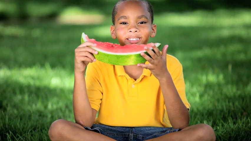Healthy young african american boy enjoying a refreshing slice of water melon in his garden