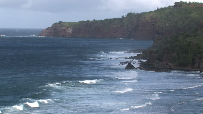 Rocky shoreline on the island of Maui in Hawaii.  Beautiful water with cliff and trees overlooking water. Waves splashing on rocks, scenic, relaxing and calm, tropical video. 
