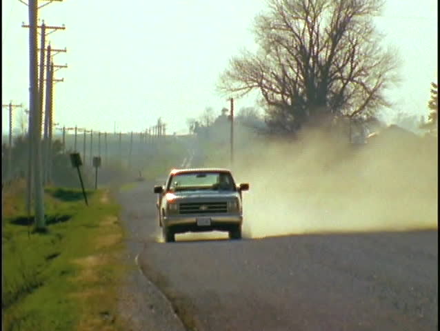 A pickup truck drives down a dirt road.