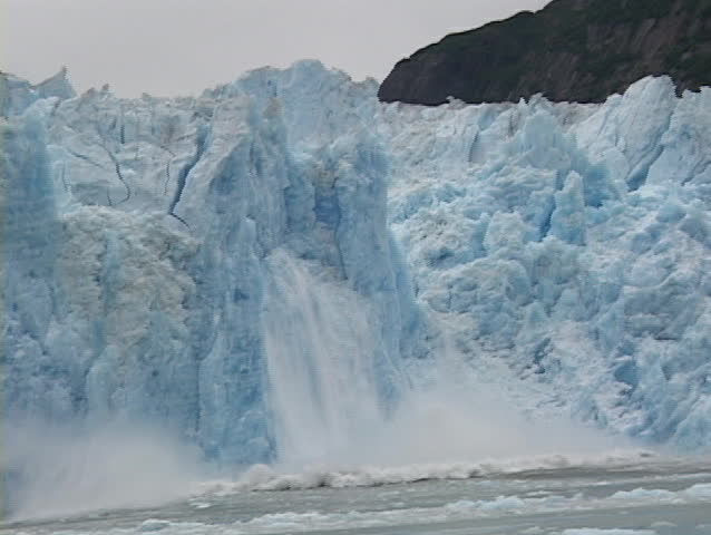 A blue wall of ice falls off an iceberg.