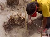 Medium-shot of an archaeological worker carefully brushing dirt from a site containing a human skull.