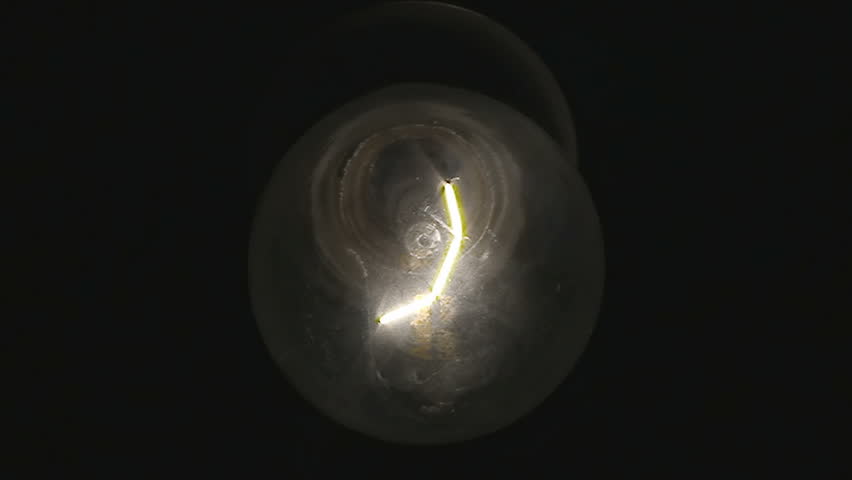 A light bulb gets turned on and off repeatedly. We can see the detail of the glass and the filament wire.