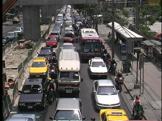 Motorcycles and bicycles work their way through gridlocked traffic on a busy street in Bangkok Thailand.