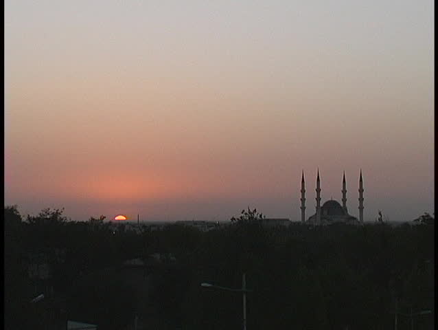 A mosque and minaret silhouette against the pink sky at golden hour.