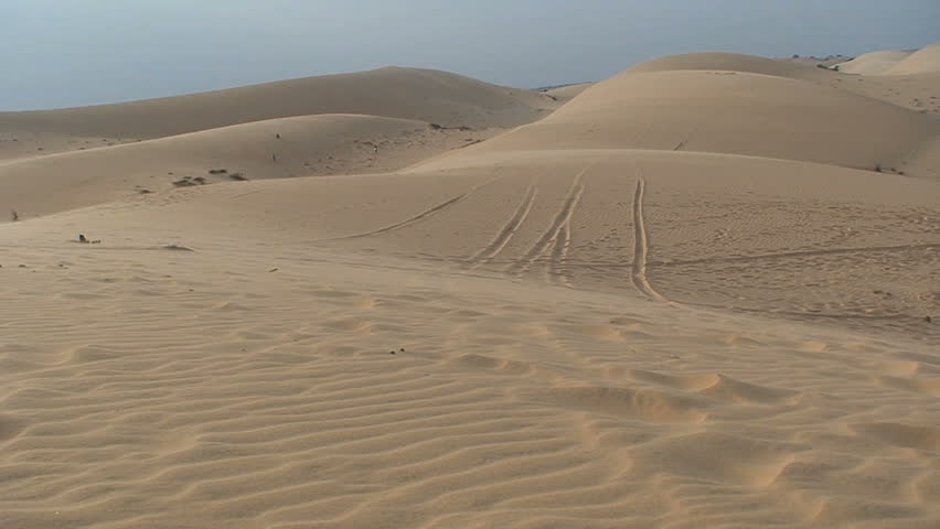 A motorcycle rides across sandunes
