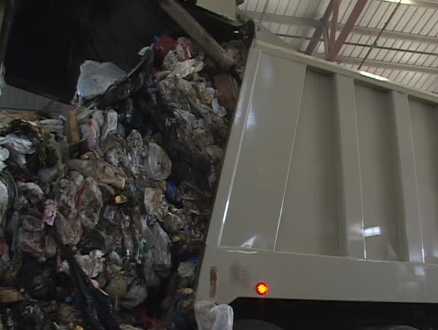 A recycling plant worker places scraps into a garbage can.