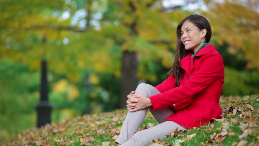 Fall woman enjoying autumn park sitting in the grass with leaves. Beautiful young mixed race Asian caucasian female model outdoors.