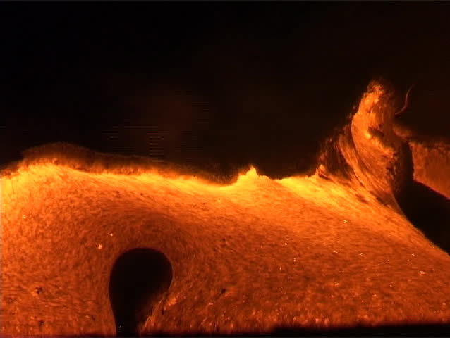 Molten lava oozes from a volcano, erupting eerily into domes belching flames.