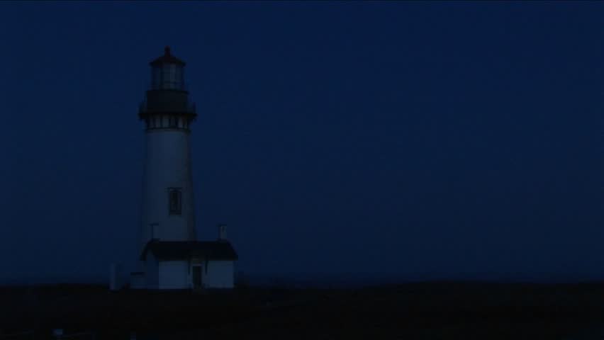 Medium shot of lighthouse at night with its bright beacon signaling a warning to passing ships.