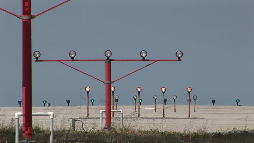 A 747 jet lands on an airport runway behind lights and guide beacons