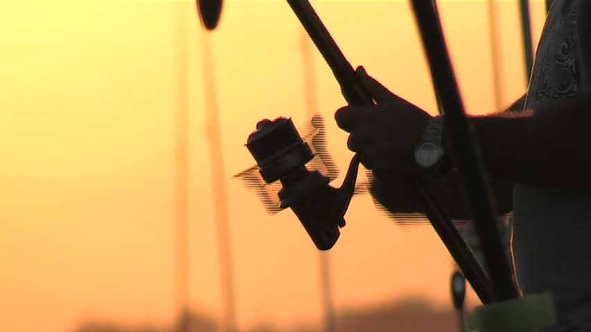Fisher recovering fishing line with reel at sunset.