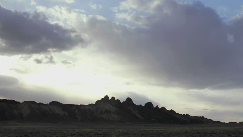 Wispy gray and white clouds pass over a mountain summit at golden hour.